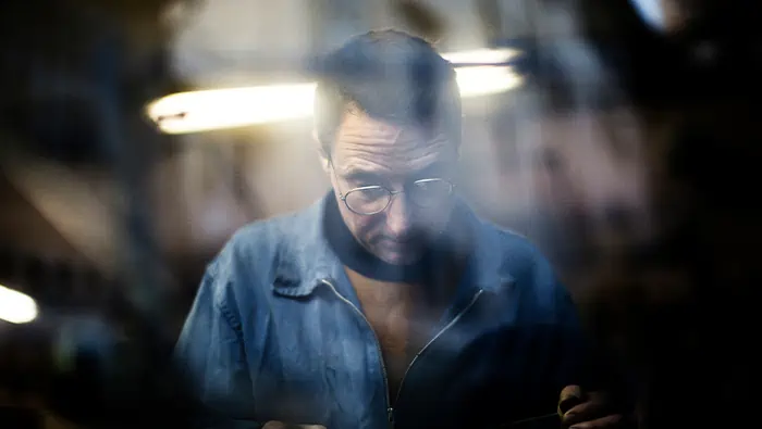 Un hombre vestido de azul tras una ventana, trabajando en un taller.