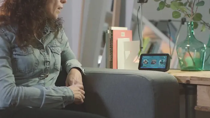 Una mujer sentada en un sofá mira un dispositivo de pantalla colocado sobre una mesa.