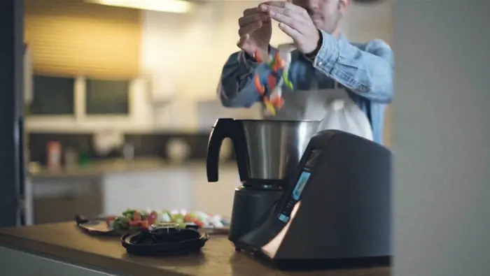 Un hombre tira verduras dentro la jarra de un robot de cocina.
