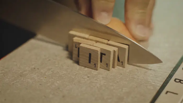 Hombre cortando fichas de madera con letras impresas usando un cuchillo.